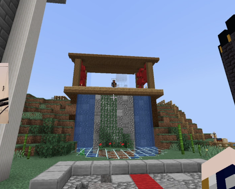 This is a screenshot from Tommy's stream. It's the L'manberg podium. It's built into the side of a hill outside of L'manberg. The bottom portion in the hill is made of cobblestone and intermitten stone bricks. The top portion is made from wood and has a roof. The sides of the stage remain open, but there are red curtains and ribbons made from the crimson forest blocks. Two water streams run down the stone work into a small pond beneath the podium. The pond is covered with glass to prevent people from falling in. There are vines that grow in the middle of the stone work between the fountains. Schlatt stands alone on the stage, looking down at the audience. Parts of other builds are barely in frame, inlcuding the L'manberg walls. The background is made of various Minecraft plants and blocks like leaves, bamboo, and poppies.