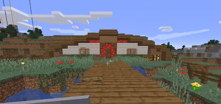 This is a screenshot of George's stream. It shows his house that he built. It's built into the side of a short hill, only barely tall enough for a player to fit inside. The walls are made of white concrete. Red spotted mushroom blocks make up a doorframe around the oak door. The roof extends from the dirt and is made of oak slabs. There is a small oak bridge over a small pond out front of his house.