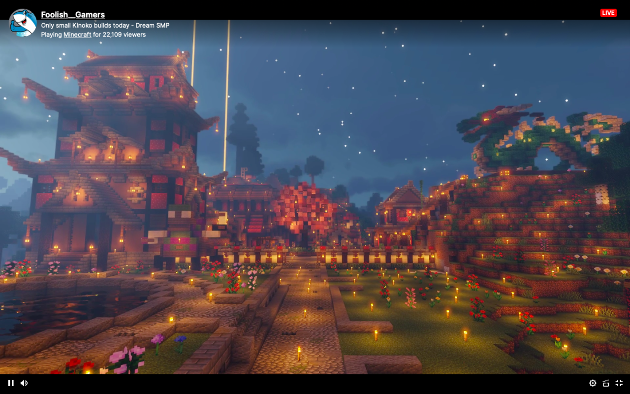 A screenshot from Foolish's stream. He's showing off Kinoko Kindom with shaders on. The ground is covered in torches to prevent mobs from spawning, but otherwise, it's beautiful. On the left stands a multi-level red building taking inspiration from a Japanese flower garden. In front of it sits a pond. Cobblestone paths connect the other smaller red houses made out of mushrooms and a giant pink cherry blossom tree. To the right sits a beautiful green (European) dragon, its eyes glowing in the dark.